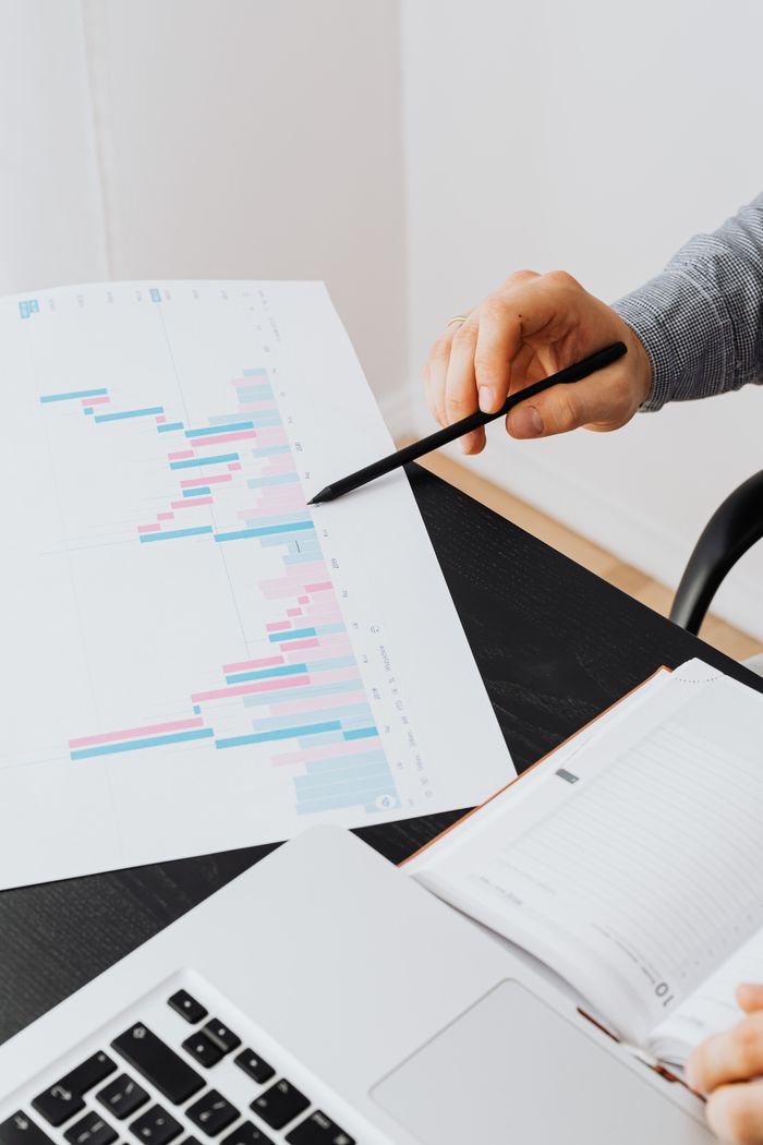 A professional analyzing data charts on paper with a laptop in an office setting.