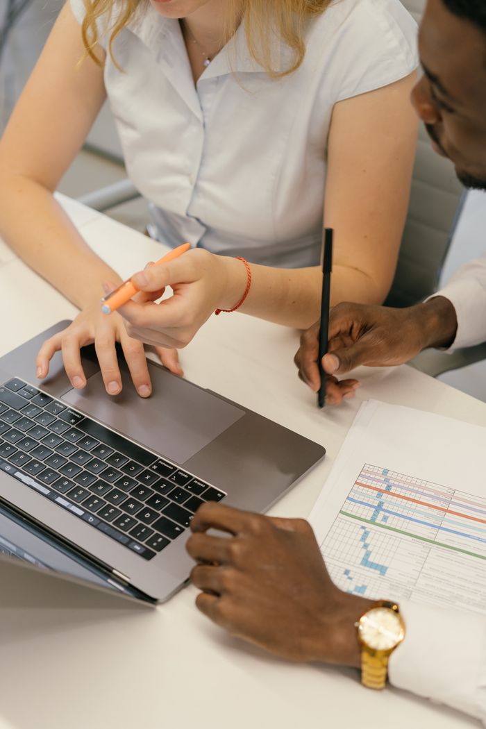 Two colleagues collaborating over a laptop and charts in an office setting.